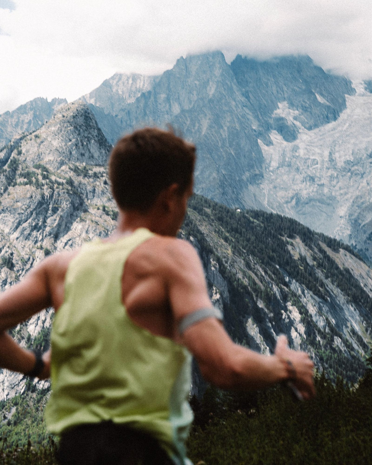 Trail runner in a yellow vest heading towards snowy mountains